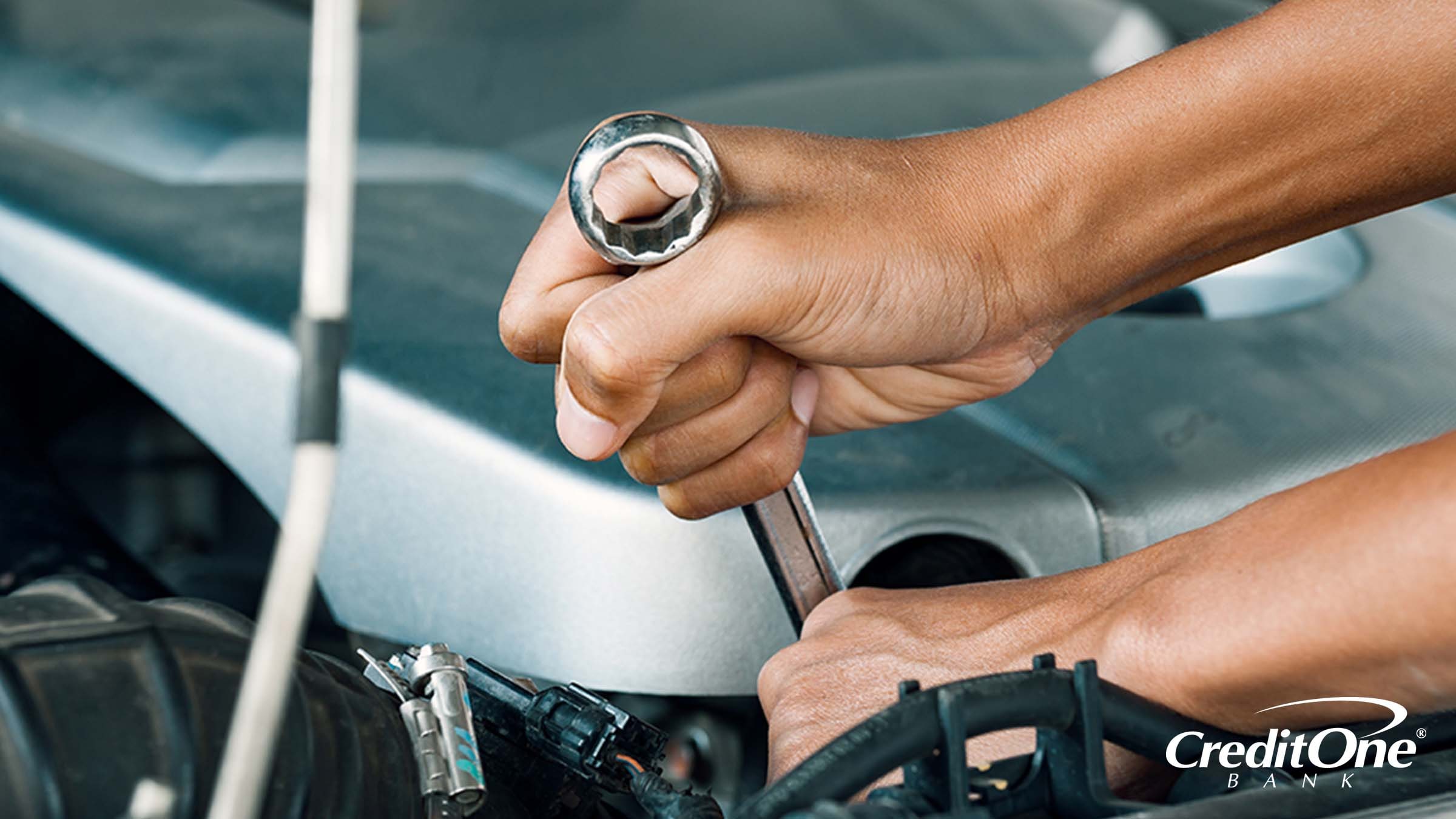A pair of hands using a wrench to apply a quick repair to a car engine